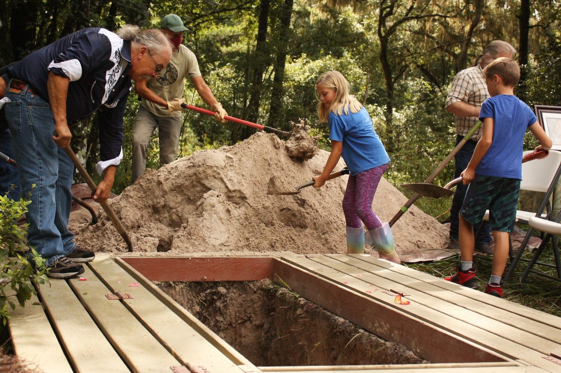A family helps to fill the grave of a loved one. There are three men and two children in the picture.